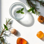 Glass with water and mint surrounded by a cedar leaf representing the olfactory notes of the perfume.